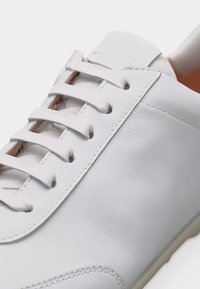 Κοντινό πλάνο ενός λευκού δερμάτινου αθλητικού παπουτσιού με λευκά κορδόνια, ορατή ραφή και ομαλή υφή επιφάνειας.