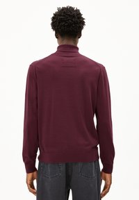 Bordeauxroter gestrickter Pullover mit hohem Kragen, gerippten Bündchen und Saum sowie einem strukturierten Patch auf der Rückseite. Weiches Material mit glatter Oberfläche.