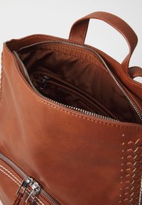 Intérieur d'un sac à dos en cuir marron avec des compartiments zippés, texture lisse et couture décorative le long du bord extérieur.