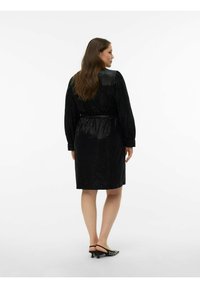 Robe noire à sequins avec manches longues, taille cintrée et coupe au niveau des genoux, présentant une texture lisse et une silhouette légèrement évasée.