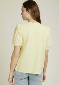 Blouse jaune à manches courtes bouffantes avec des broderies. Tissu doux avec une finition en dentelle sur les bords. Design simple et ample.