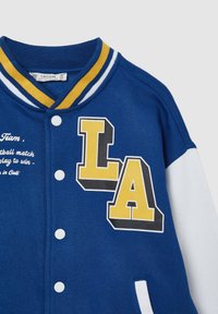 Niebieska kurtka varsity z żółto-czarną naszywką "LA", białymi rękawami i paskowanym kołnierzem. Zapięcia na guziki oraz szczegóły z tekstem.