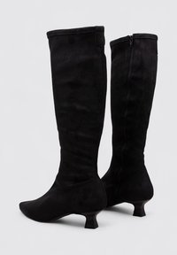 Botas negras hasta la rodilla hechas de suave ante, con una punta estrecha y un tacón bajo y contundente. El diseño incluye un cierre de cremallera lateral.