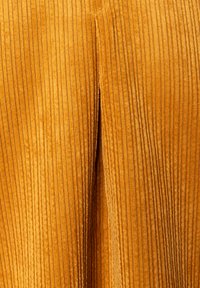Senfgelber Cordstoff mit vertikalen Streifen und einem leichten Schlitzdetail in der Mitte, das Textur und Wärme zur Schau stellt.