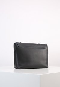 Borsa a tracolla in pelle nera con una superficie liscia, forma rettangolare, chiusura a patta superiore e dettagli di cucitura sottili. Design semplice e funzionale.