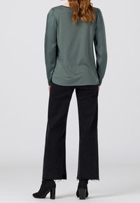 Top a maniche lunghe color turchese con dettagli arricciati sulle spalle abbinato a pantaloni neri a gamba larga con orli sfilacciati e stivaletti con tacco alto.