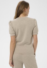 Beżowa bluzka krótko rękawowa z okrągłym dekoltem i subtelnymi bufkami na ramionach, wykonana z miękkiego materiału, w zestawie z pasującymi beżowymi dołami.