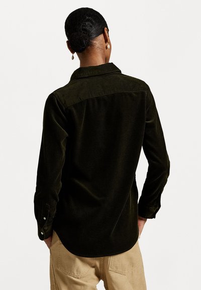 Dark green corduroy shirt with a curved hem, long sleeves, and button cuffs. Features a rounded collar and textured fabric.
