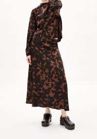 Henkilö pukeutuneena mustaan ja ruskeaan abstraktiin pitkähihainen yläosa ja siihen sopiva pitkä hame, yhdistettynä mustiin niitatuihin klompeihin.