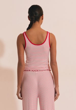 Donna con capelli intrecciati vista di spalle, indossa una canotta a righe rosse e bianche e pantaloni coordinati su uno sfondo uniforme.