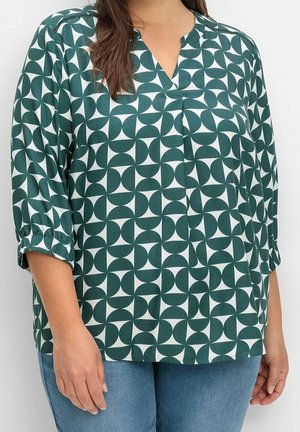 Blusa verde con estampado geométrico con detalles en blanco, escote en V y mangas tres cuartos, confeccionada en tela ligera.