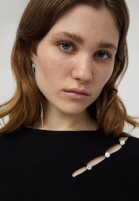 Czarny sweter żebrowany z wycięciami ozdobionymi trzema kwiatowymi aplikacjami. Długie srebrne kolczyki w stylu żyrandola dopełniają całość.