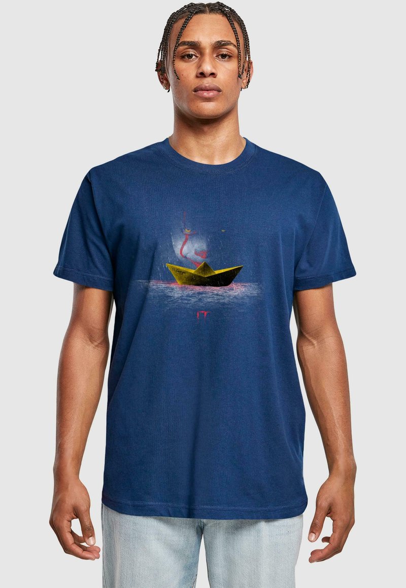 Pusauks zilas kokvilnas t-kreklu ar dzeltenas papīra laivas grafiku uz ūdens, ar sarkaniem akcentiem un smalku fona dizainu.