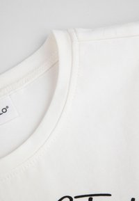 Bluza z białej bawełny w zbliżeniu, z okrągłym dekoltem, delikatną teksturą i czarnym nadrukiem. Czysty design z prostymi detalami szycia.
