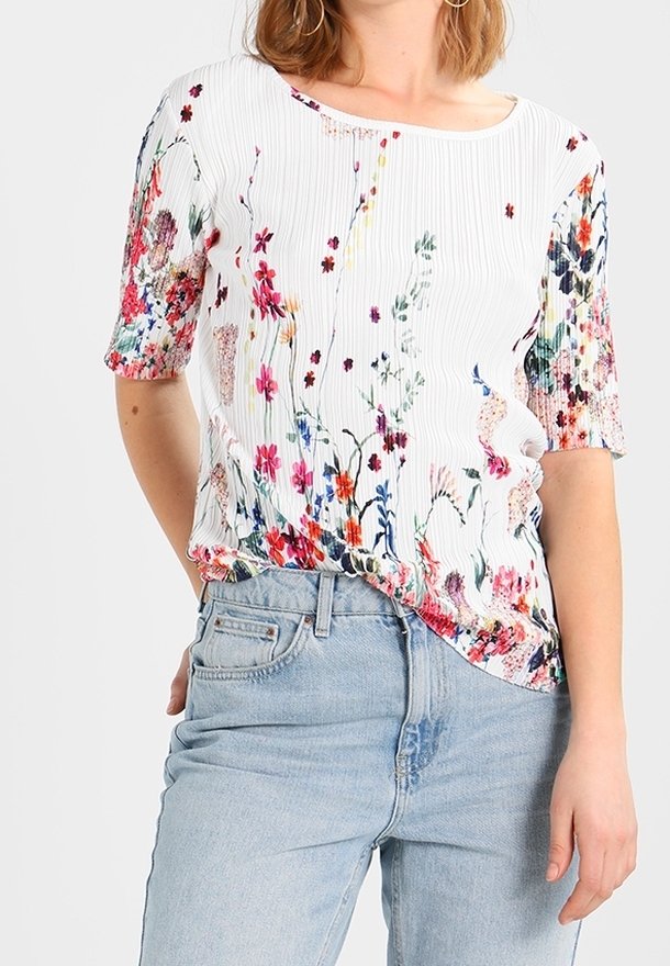 Haut blanc côtelé avec imprimé floral multicolore, manches courtes, porté rentré dans un jean taille haute bleu clair.