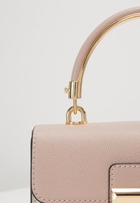 Borsa a mano in pelle texturizzata rosa con manico curvo in oro e accessori in oro. Presenta una forma rettangolare con chiusura magnetica.
