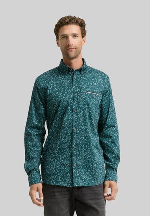 Cyaan knoopshirt met een gespikkeld patroon, lange mouwen en een borstzak met een contrasterende witte streep. Grijze achtergrond.