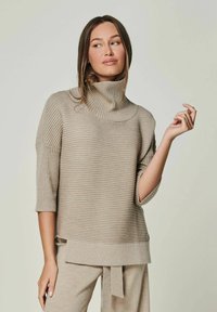 Beige gerippter Rollkragenpullover mit kurzen Ärmeln und einer lockeren Passform. Mit einem umgeschlagenen Kragen und subtiler Textur, kombiniert mit passenden Hosen.