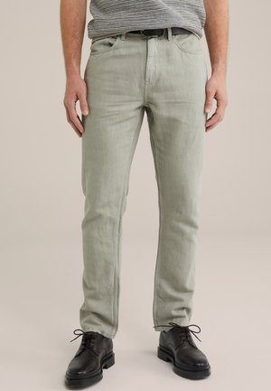 Helle grüne Baumwollhosen mit geradem Schnitt, Fünf-Taschen-Design und kombiniert mit dunklen Lederschuhen. Glatte Textur mit minimaler Detailgestaltung.