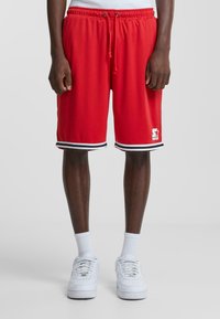 Shorts atletici roșii cu un cordon la talie, prezentând tivuri cu dungi negre și albe și un logo alb. Fabricati dintr-un material ușor.