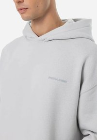 P sweatshirt cinza claro com uma textura suave, capuz com cordão e um logotipo discreto em um tom ligeiramente mais escuro na frente.