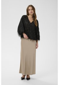 Bluza neagră cu franjuri și mâneci largi, cu decolteu în V. Asortată cu o fustă maxi bej. Pantofii negri cu vârf ascuțit completează ținuta.