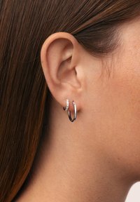 Orecchini a cerchio in argento con un cerchio più piccolo, decorato con cristalli, sopra un cerchio più grande e lucido. Texture liscia e forma circolare.