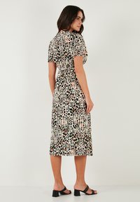 Maxi dress with a leopard print pattern in various colors, short sleeves, cinched waist, and flowing fabric, paired with black block-heeled sandals.