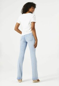 Witte t-shirt met korte mouwen, gecombineerd met lichtblauwe flared jeans, die een aangesloten ontwerp en denim textuur tonen, met casual schoeisel.
