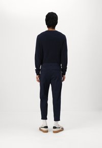 Námořnický svetr s texturovaným úpletem, kombinovaný s odpovídajícími námořnicky modrými kalhotami s bočními kapsami. Obuv: bílé boty s černými detaily a viditelnou podrážkou.