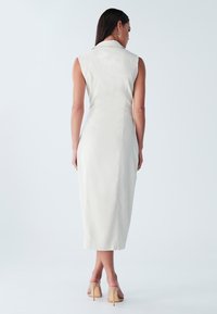 Mouwloze crèmekleurige jurk met een kraag, een aansluitende pasvorm en een zoom tot op de knie. Soepele, matte stof met een rechte snit en subtiele naden.