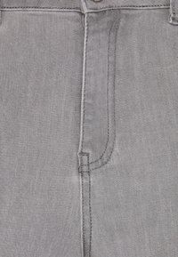 Tejido de mezclilla gris con un bolsillo frontal, costuras rectas y cierre de botón de metal en la cintura. Textura suave y acabado uniforme.