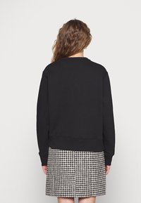 Sudadera negra con cuello redondo, puños y dobladillo acanalados. Combinada con una falda de patrón de espiga en blanco y negro.