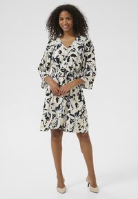 Vestito a stampa floreale con davanti a bottoni, vita cinturata e maniche a tre quarti. I colori includono crema, blu e nero. Tessuto morbido.