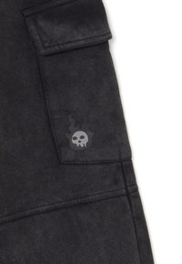 Zwarte stoffen kleding met een klepzak, voorzien van een kleine vlammenkop in grijs en zwart aan de onderrand.