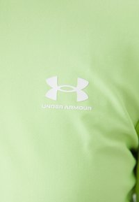 Világoszöld sportpóló, sima anyagból, fehér Under Armour logóval a középen, ami a minimalista dizájnt hangsúlyozza.