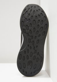 Black rubber shoe sole featuring an intricate pattern of oval cutouts, textured surface for grip, and a central logo detail.