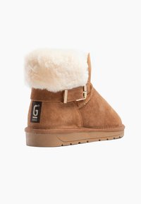 Botas de tobillo de ante marrón con un suave cuello de crema, que presentan un detalle de hebilla lateral y una suela de goma texturizada.