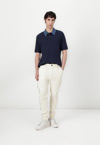 Mörkblå polo med en kontrasterande ljusblå krage, tillsammans med krämfärgade kordbyxor med sidostripes, och vita sneakers.
