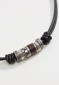 Schwarzes Lederhalsband mit Metallperlen in unterschiedlichen Texturen und einer Holzperle, akzentuiert mit gravierten Buchstaben und kreisförmigen Mustern.