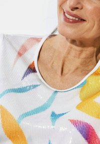 Witte top met korte mouwen, versierd met kleurrijke abstracte patronen in oranje, geel, blauw en paars, met pailletten voor extra textuur en glans.