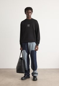 Sorte genser med logo-patch, kombinert med blå patchwork jeans. Sort totebag og svarte ankelstøvler fullfører antrekket.