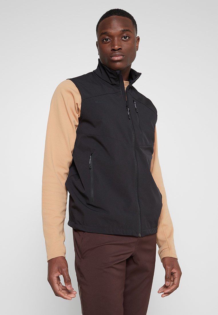 Schwarze zip-up Weste mit Stehkragen, Fronttaschen und schlankem Design, getragen über einem hellen Langarmhemd, kombiniert mit braunen Hosen.