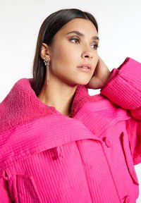Giacca rosa trapuntata con colletto peloso, dotata di grandi bottoni e tasche. Accessoriata con un orecchino a forma di stella e labbra lisce e lucide.