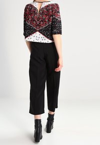 Blusa floreale bianca e nera con maniche corte, chiusura con zip sul retro; abbinata a pantaloni neri cropped e stivaletti neri con tacco.