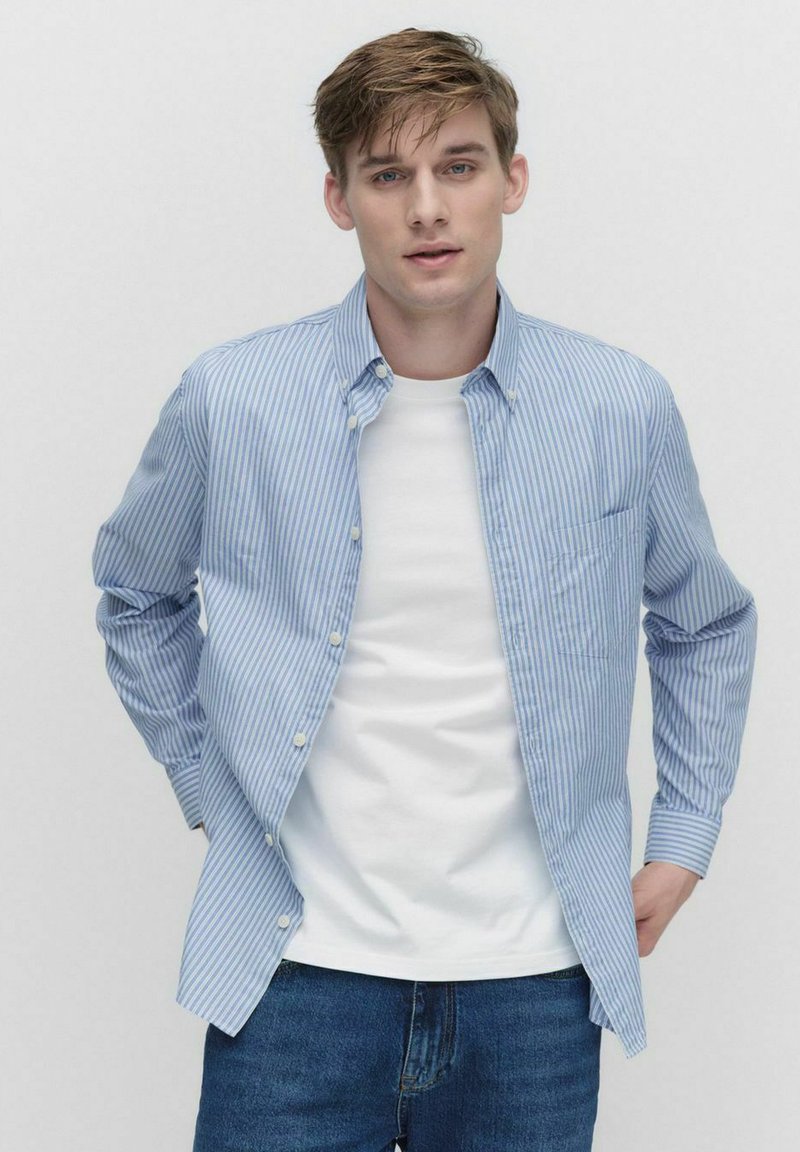Blå og hvidstribet skjorte med knapper, blød krave, brystlomme og afslappet pasform over en hvid t-shirt; båret med denim jeans.