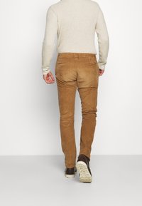 Bruine corduroy broek met een slanke pasvorm, voorzien van achterzakken en een zachte textuur. Gecombineerd met donkere schoenen en een lichte trui.