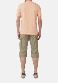 T-shirt en coton pêche clair et shorts cargo verts olive avec poches latérales, portés avec des chaussures de sport beiges et marine. Design simple, coupe décontractée.
