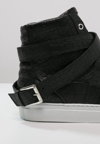 Czarne wysokie trampki z teksturą skóry krokodyla, bocznym paskiem i srebrną klamrą. Posiadają białą gumową podeszwę i elegancki design.