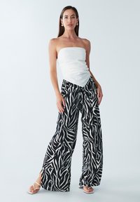 Witte strapless top met een gegarneerde textuur, gecombineerd met zwart-witte wijde broek met zebraprint. De look wordt compleet gemaakt met witte sandaaltjes met bandjes.